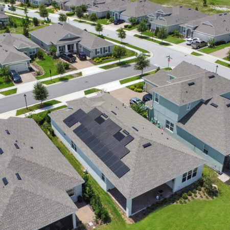 Zoomed out aerial view of a Deland, FL home with solar panels on the roof within a residential neighborhood.